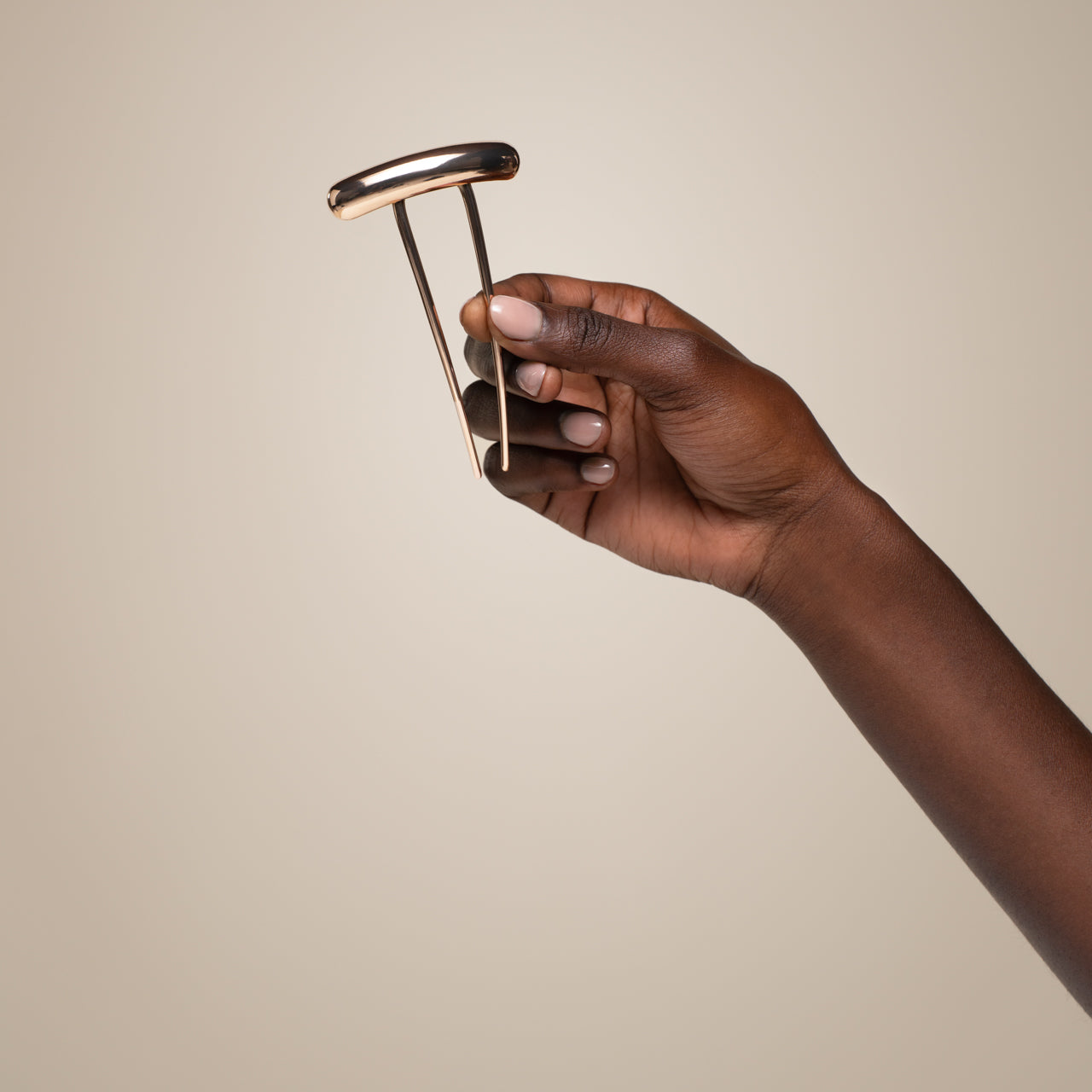 Hand holding a gold barrette french hair pin against a beige background