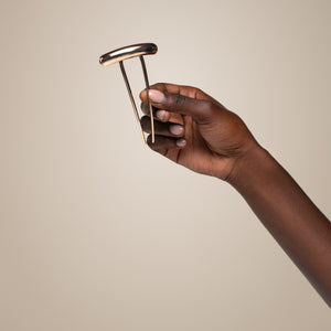 Hand holding a gold barrette french hair pin against a beige background