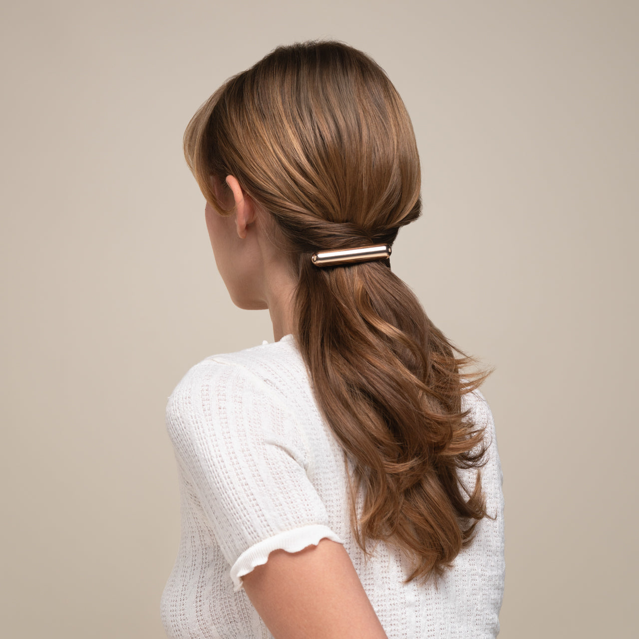 Woman with a ponytail held by a hair clip against a neutral background