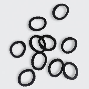 Kitsch black ribbed hair ties scattered on a light gray background