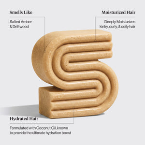 A beige, textured hair shampoo bar shaped like a stylized letter 'S' on a light gray background, with text callouts describing its scent and hair benefits.
