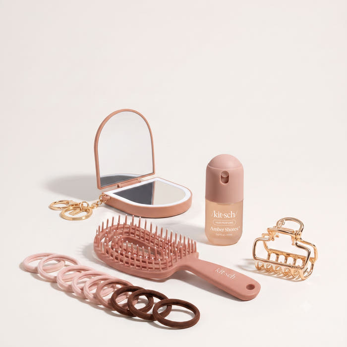 Rush On The Go Kit flat lay including Kitsch compact mirror with keychain, travel-size hair mist, mini paddle brush, gold claw clip, and elastic hair ties in mauve and brown tones on a neutral background
